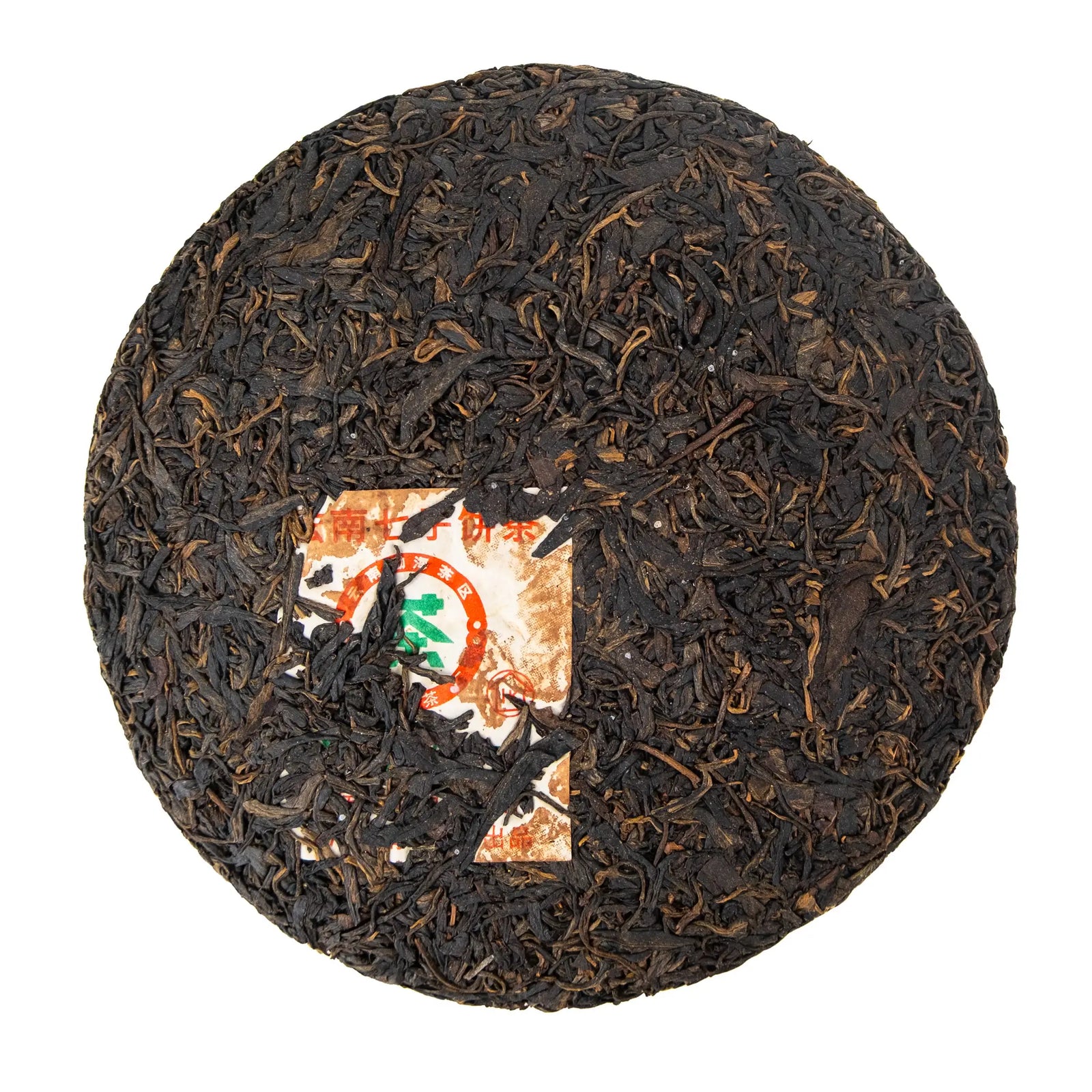 Unwrapped 2012 Nanqiao Selection raw puerh cake showing dark compressed leaves and the paper ticket pressed into the cake