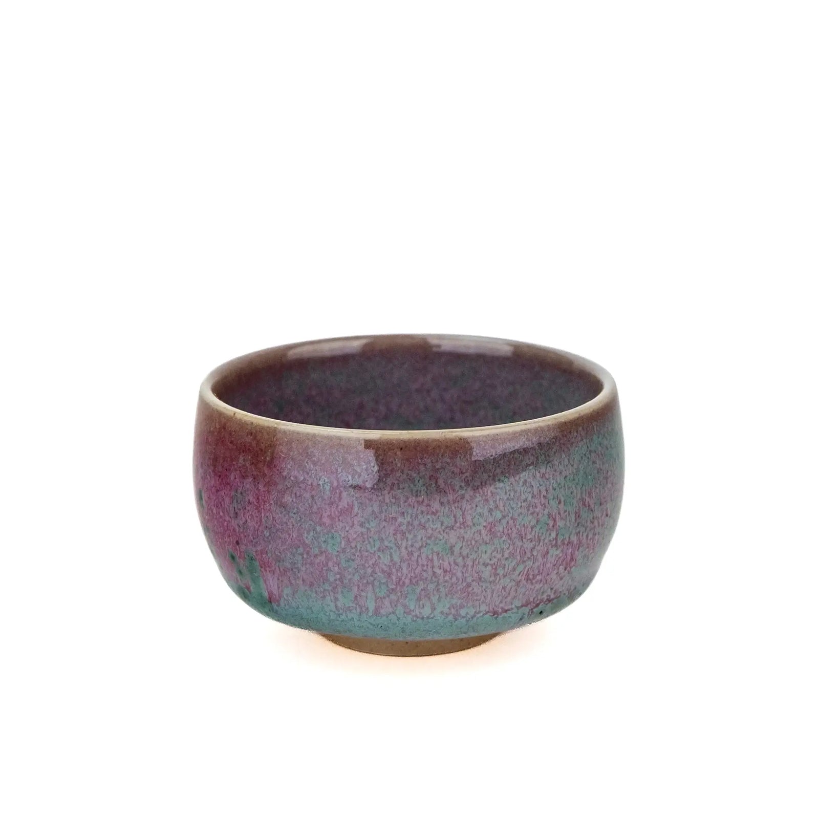 A handmade ceramic teacup with a glossy glaze featuring a gradient of purple, pink, and teal-green, with a natural brown clay base, set against a plain white background.