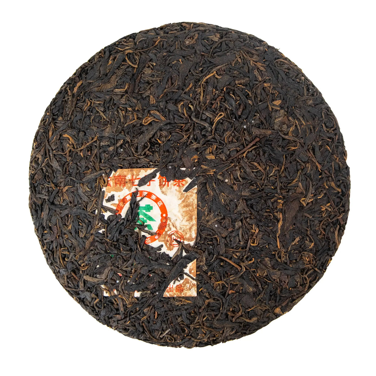 Unwrapped 2012 Nanqiao Selection raw puerh cake showing dark compressed leaves and the paper ticket pressed into the cake