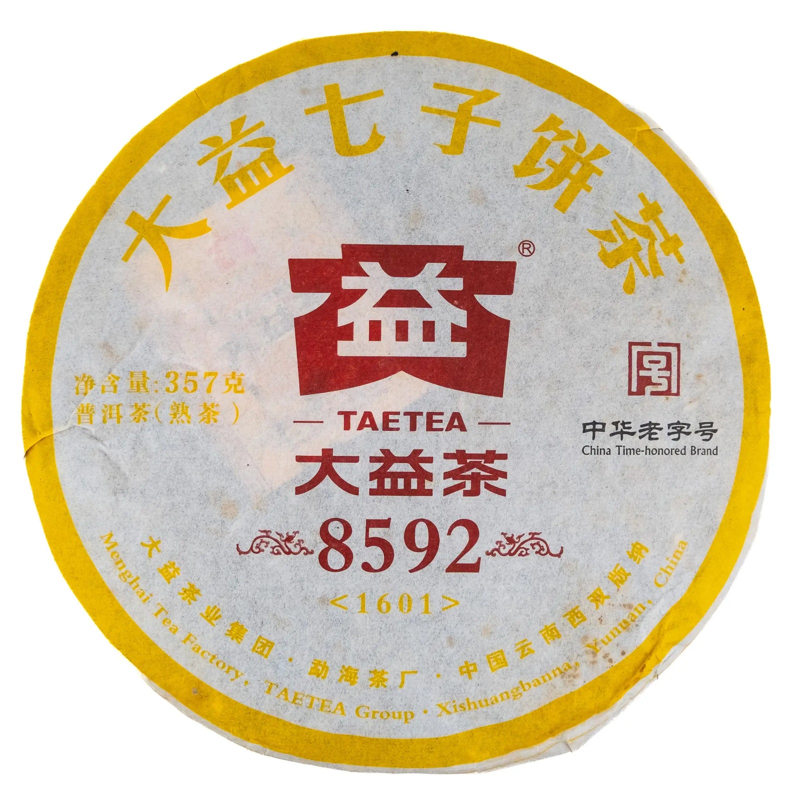 A round cake of 2106 Dayi 8592 ripe puerh with a yellow, white, and red wrapper on a white background.