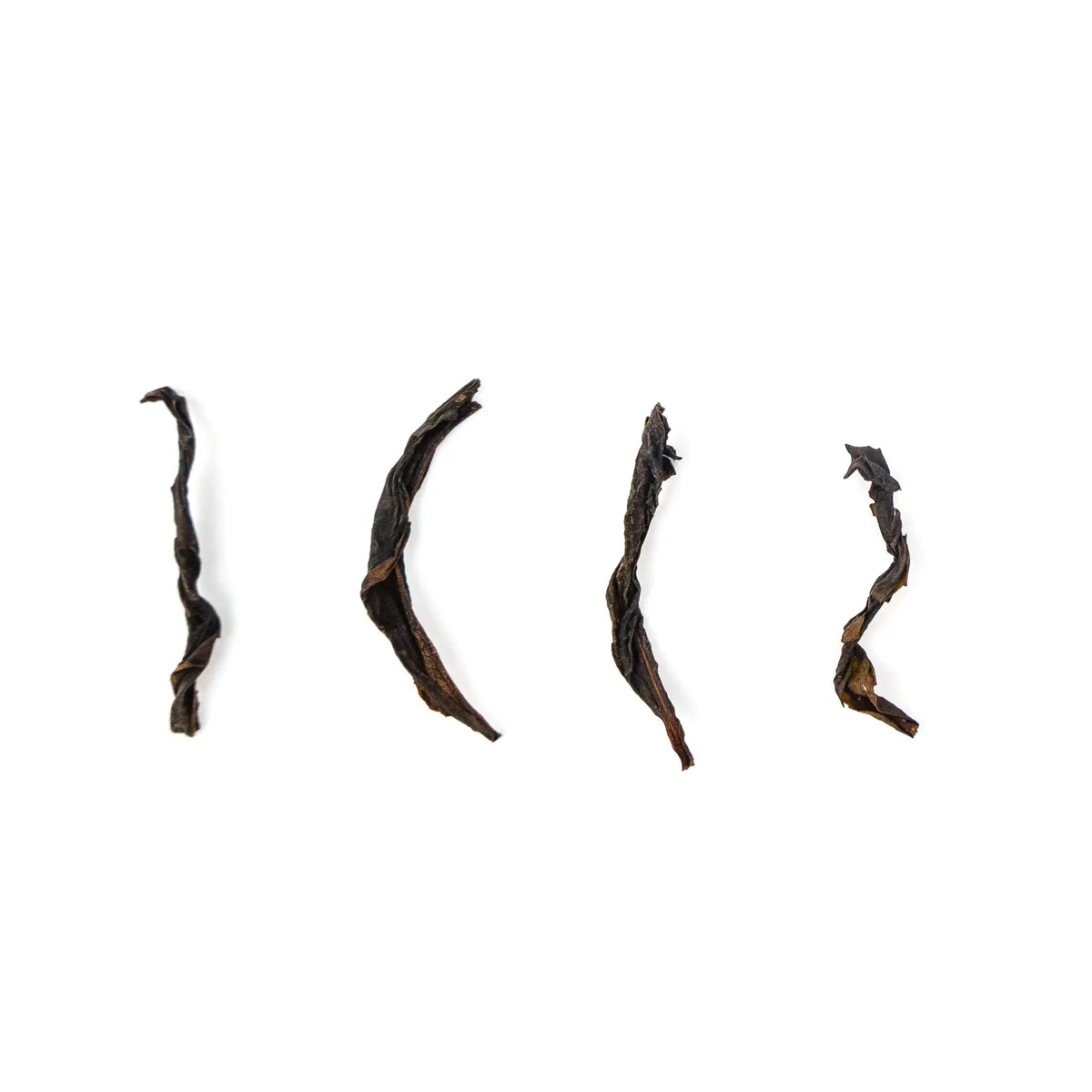 Four long, curved dark leaves of Wildflower Phoenix oolong spaced out on a white background