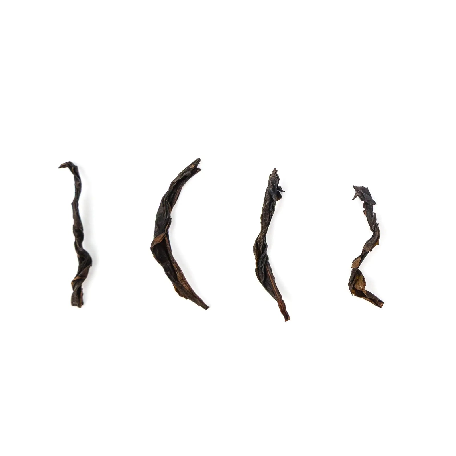 Four long, curved dark leaves of Wildflower Phoenix oolong spaced out on a white background