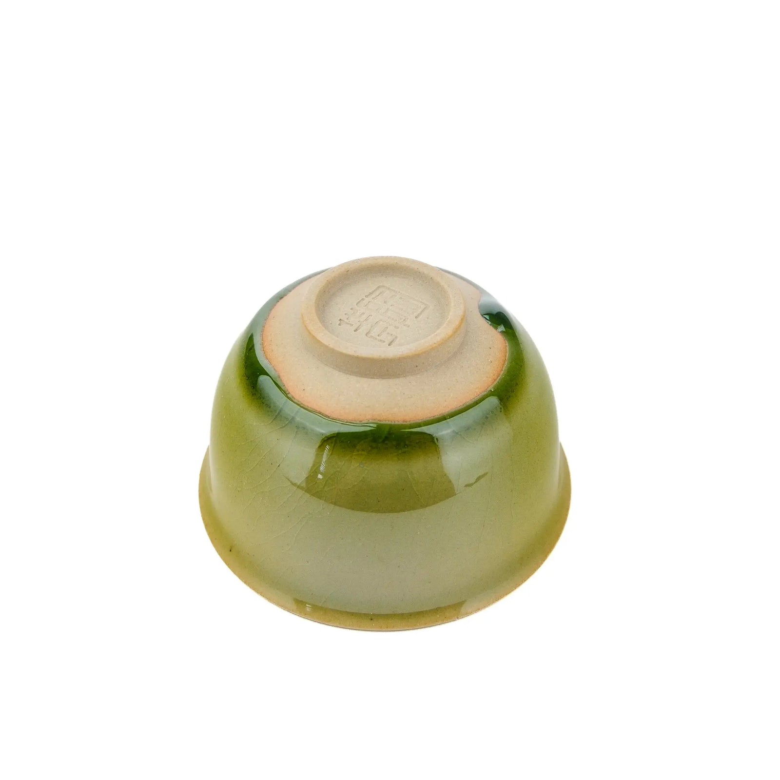 Underside view of a small handmade tea cup for gong fu tea with a green glaze but unglazed tea cup foot