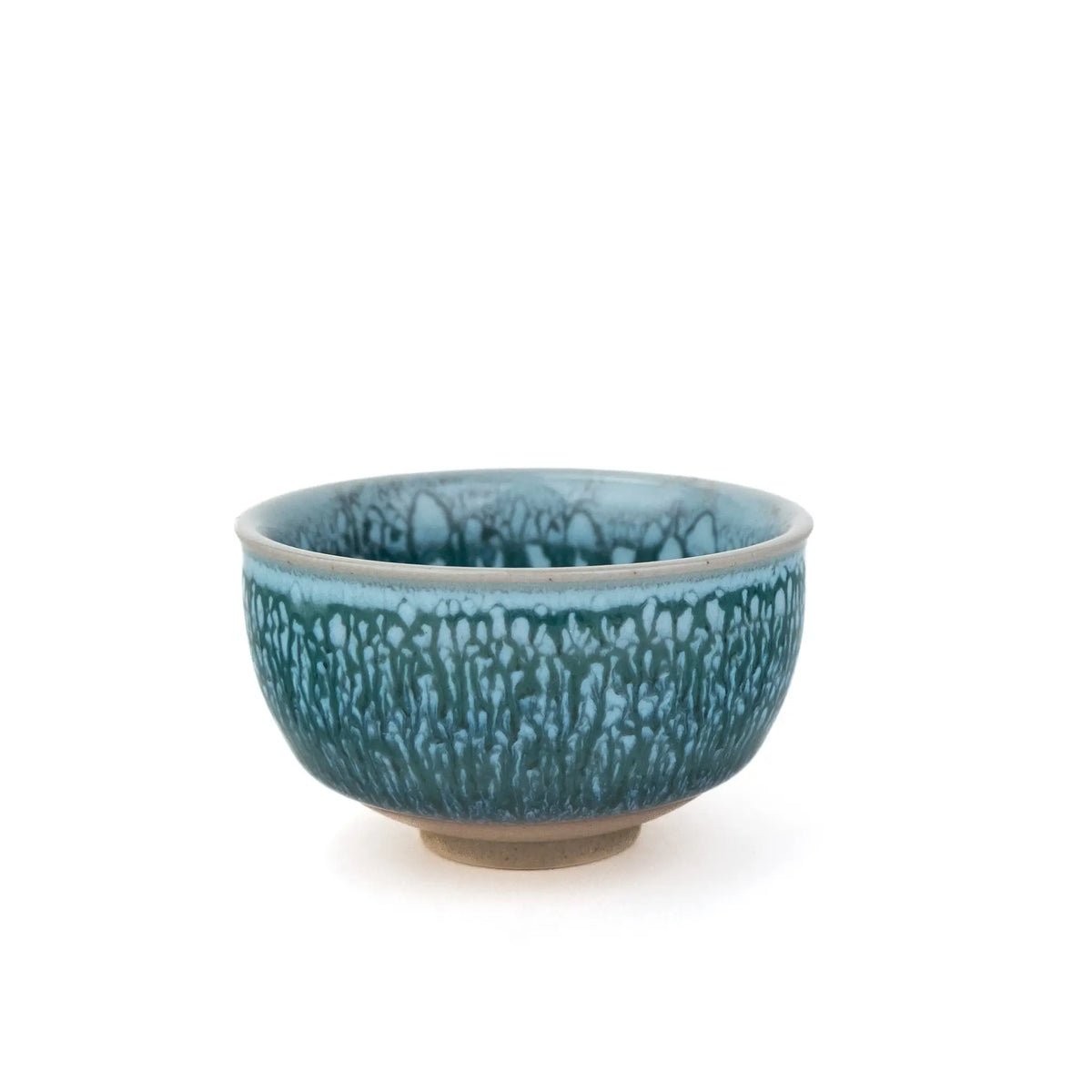 A ceramic tea cup with a textured, dripping glaze in shades of teal and blue, featuring a natural clay foot, set against a plain white background.