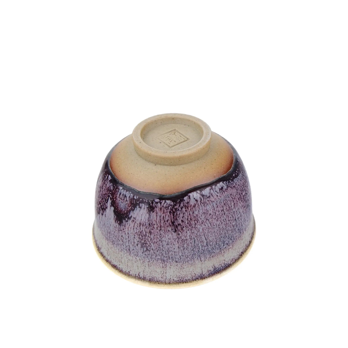 A single ceramic handmade teacup with a glossy glaze, photographed from above on a plain white background. The bowl is upside down, showing the unglazed clay base with a small stamped mark in the center.