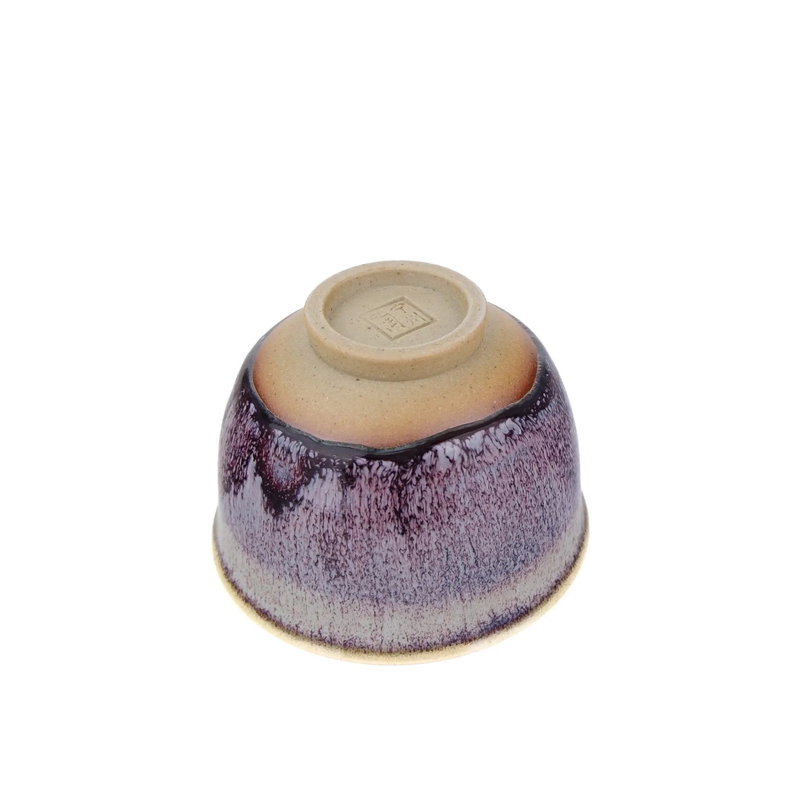 A single ceramic handmade teacup with a glossy glaze, photographed from above on a plain white background. The bowl is upside down, showing the unglazed clay base with a small stamped mark in the center.