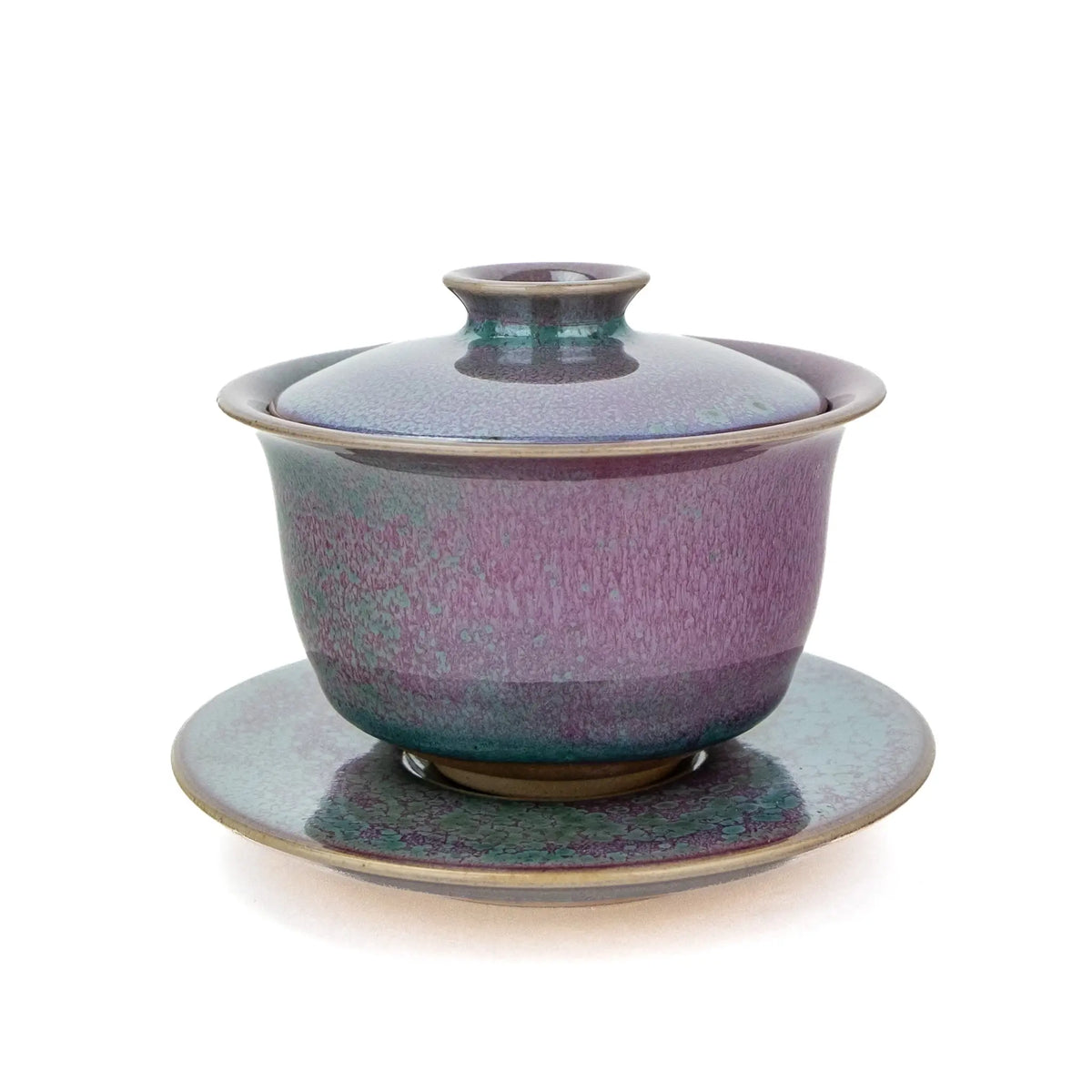 A ceramic handmade gaiwan with a matching saucer, featuring a speckled glaze that transitions from teal green to deep magenta , set against a plain white background.