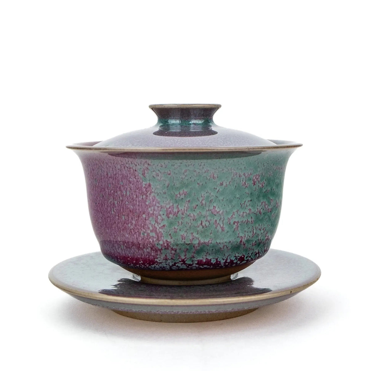 A ceramic handmade gaiwan with a matching saucer, featuring a speckled glaze that transitions from teal green to deep magenta , set against a plain white background.
