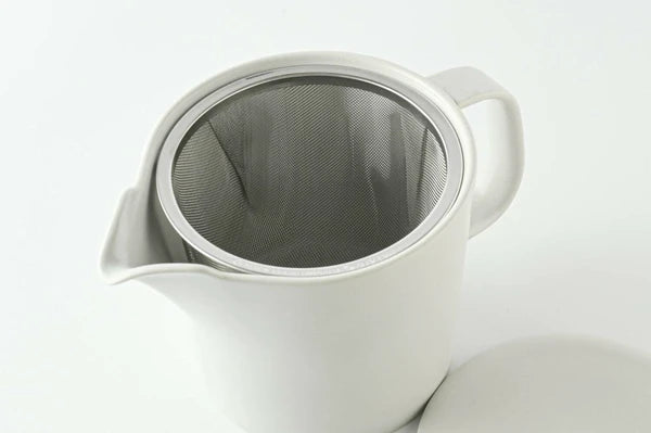 Light grey ceramic teapot with a metal mesh filter on a white background