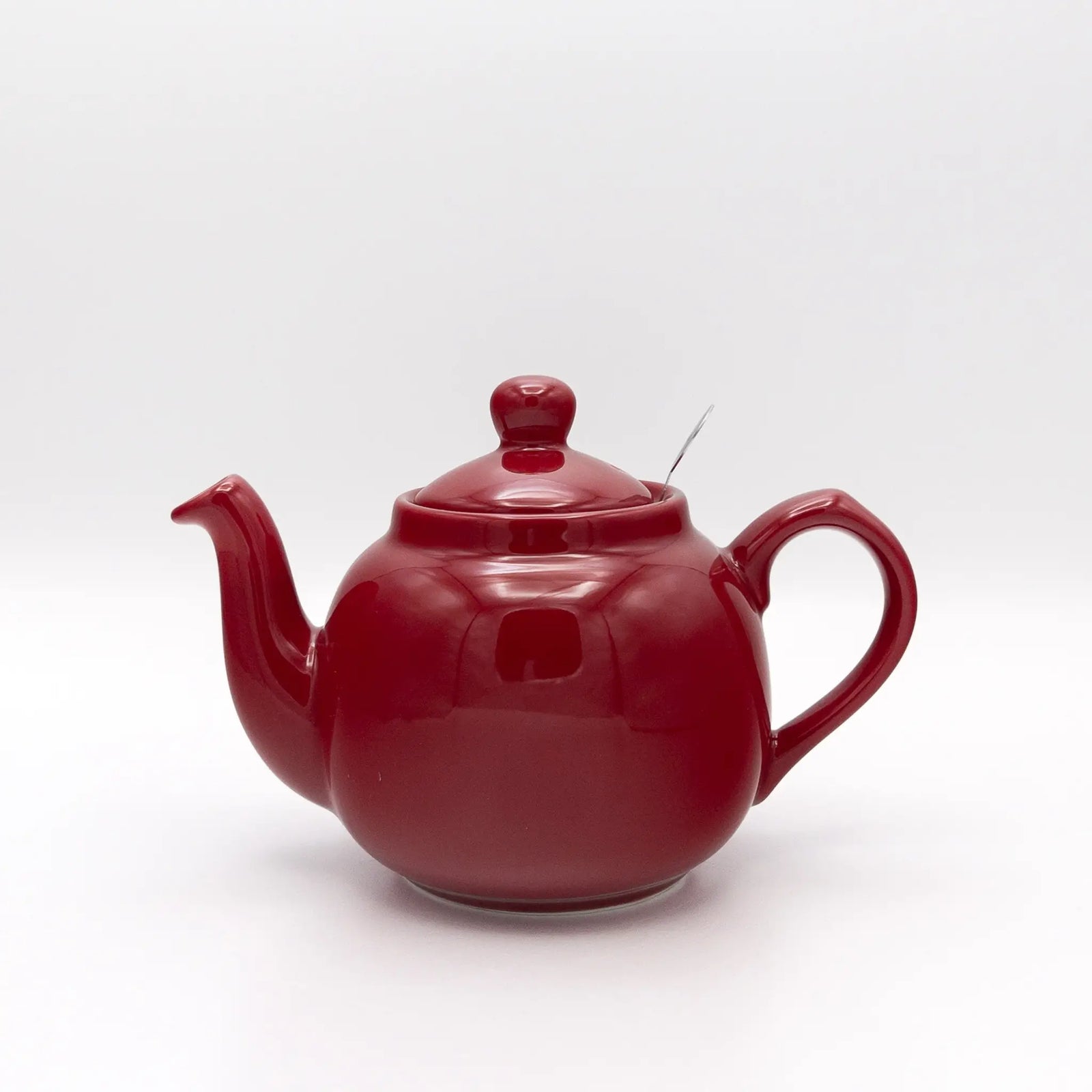 A glossy dark red ceramic teapot with a matching lid, shown on a plain white studio background.