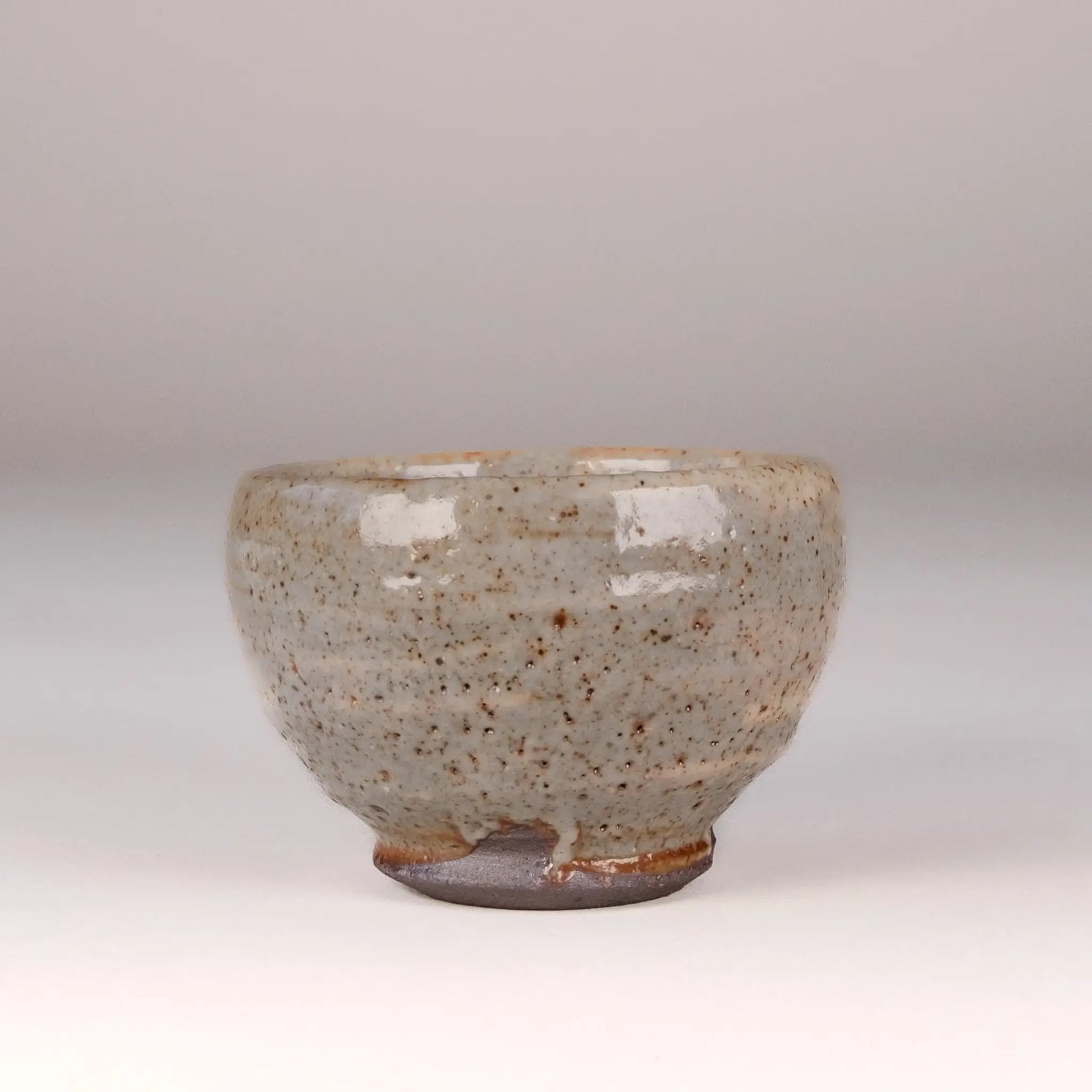 Ceramic handmade tea cup with speckled glaze on a plain background