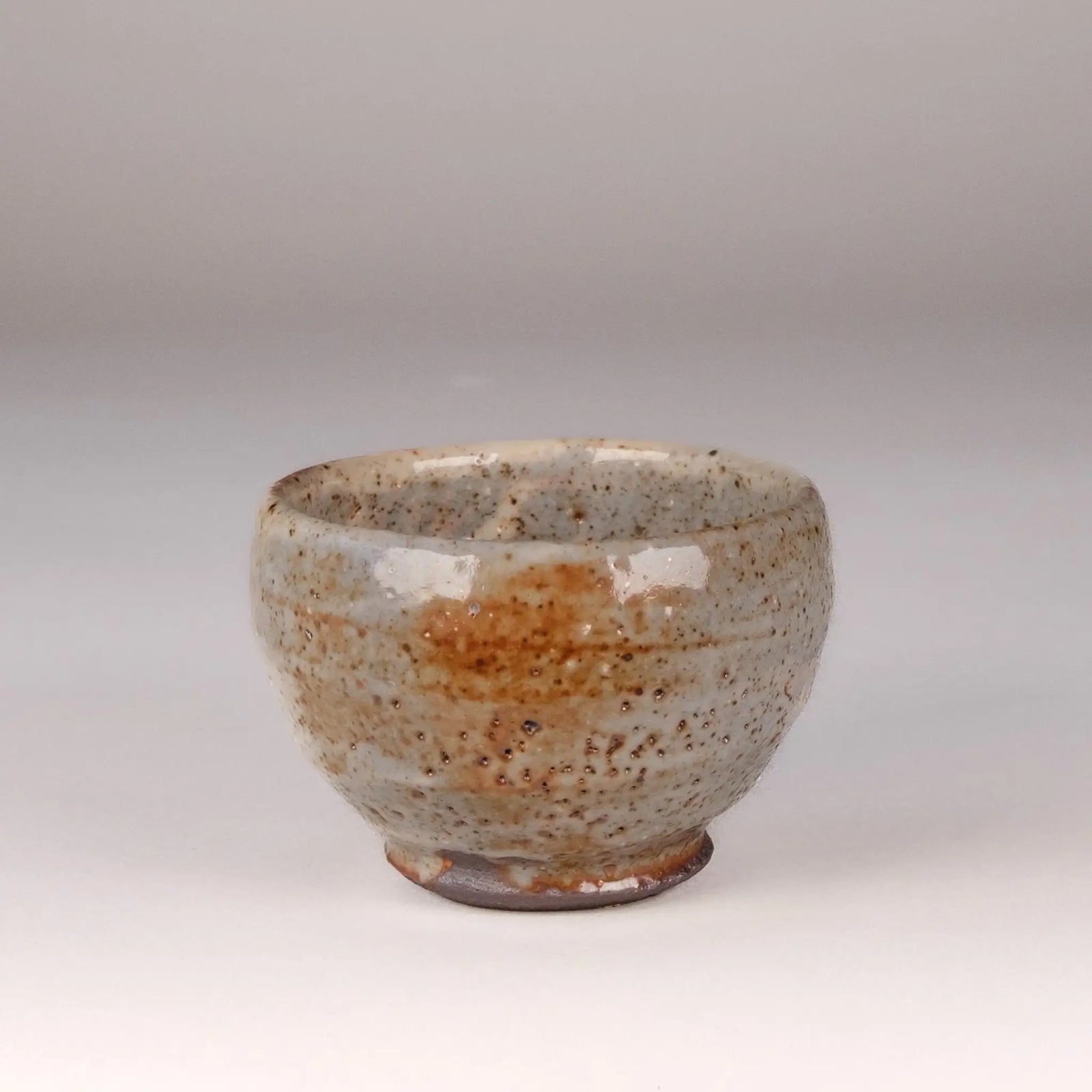 Ceramic handmade tea cup with speckled glaze on a plain background