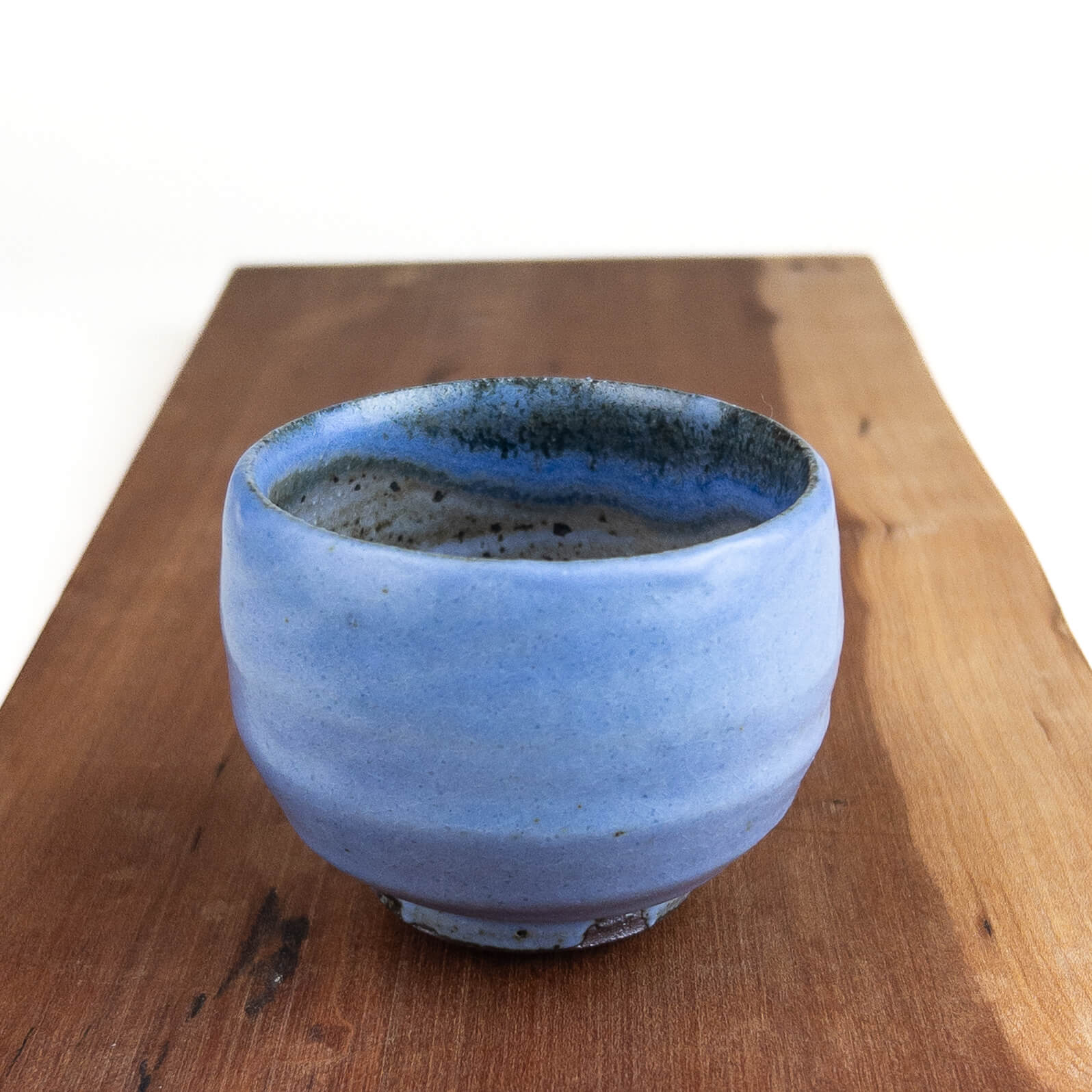 Blue ceramic cup on a wooden surface with a white background