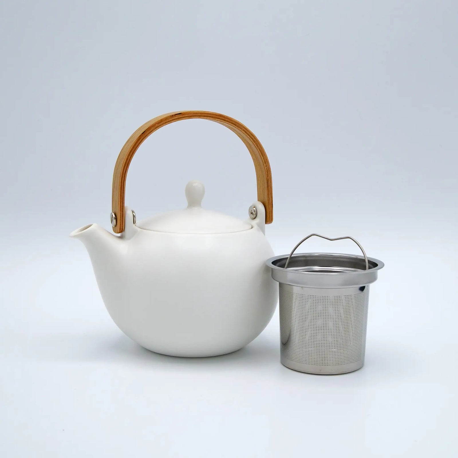 White teapot with wooden handle and metal tea infuser on a light gray background