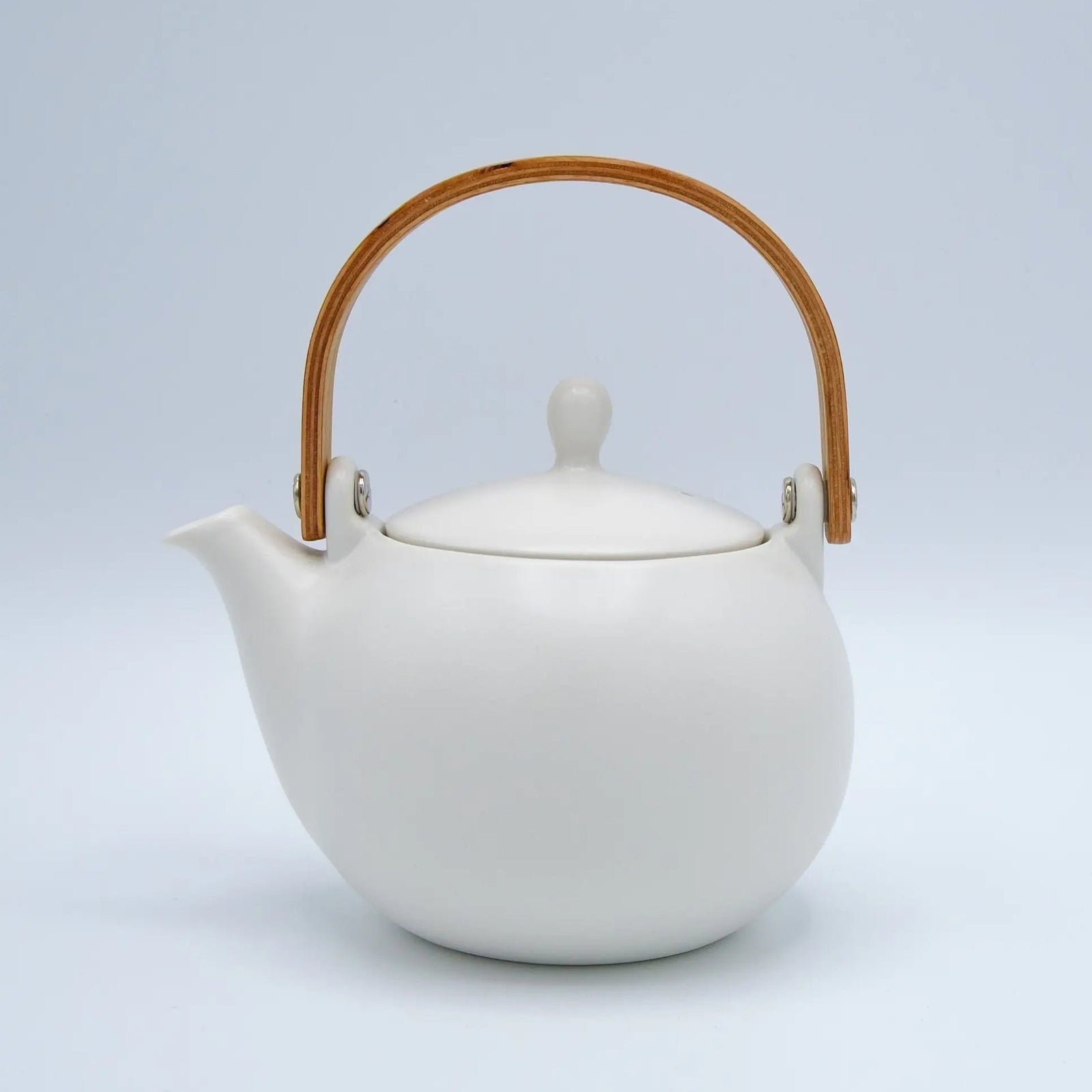 White ceramic teapot with a wooden handle on a light gray background