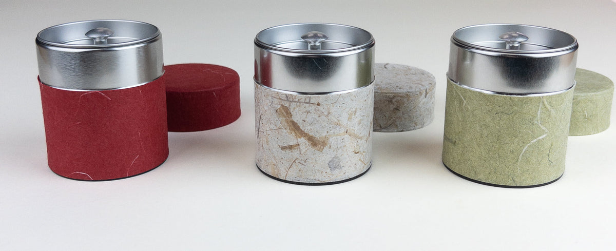 Set of cylindrical tea containers with metal lids on a white background