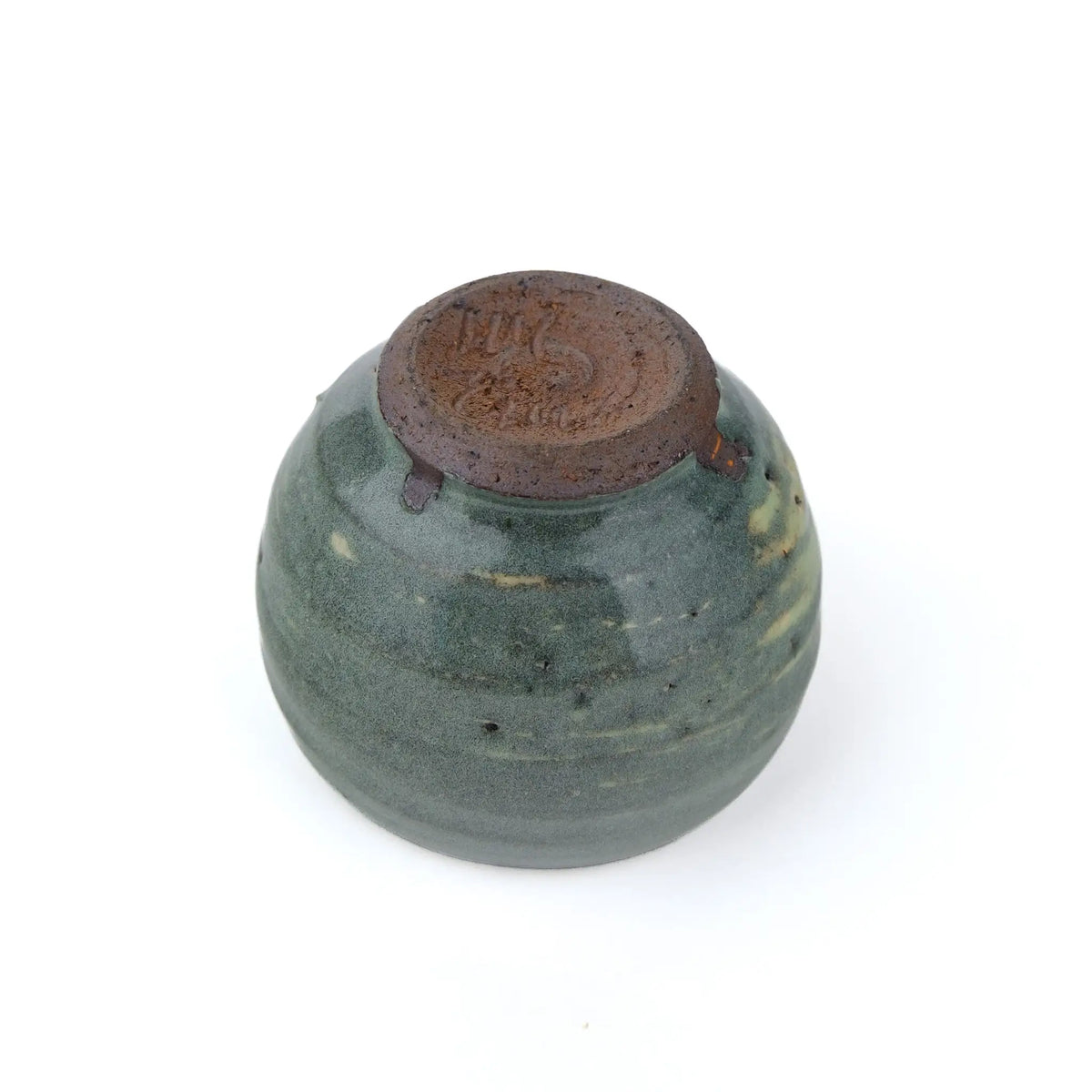 Mark Mohler handmade tea cup #B turned upside down, showing the unglazed reddish brown foot with marks carved into it and throwing rings in the green glaze